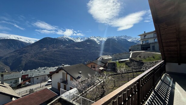 Blick auf Berge mit schneebedeckten Gipfeln, einem klaren Himmel und eine Wohngegend mit Gebäuden und einer Straße.