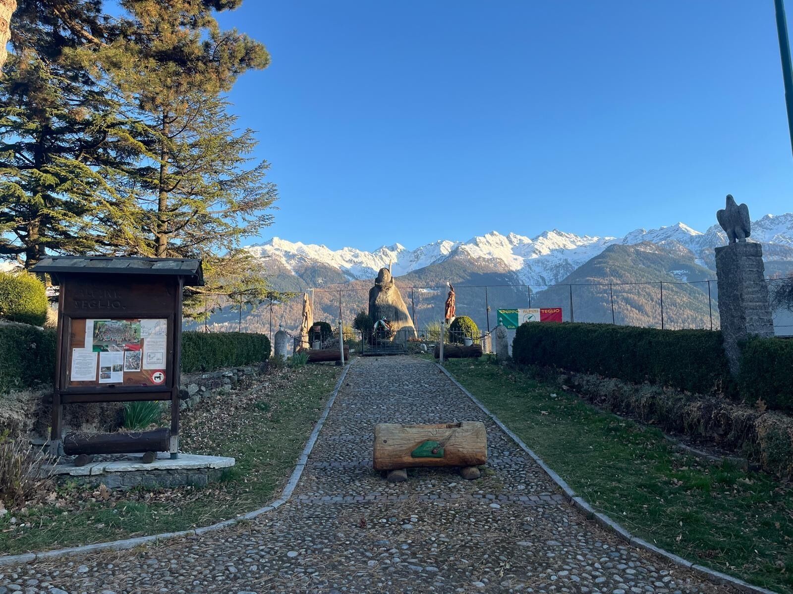 Un sentiero conduce a una vista sulle montagne, con una statua e un cartello.
