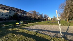 Ein Park mit Spielgeräten, Bänken und einem Gebäude im Hintergrund.