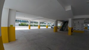 Un vaste parking souterrain avec des piliers jaunes et blancs, un escalier et un extincteur.