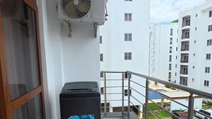 Un balcon avec une poubelle, un appareil de climatisation et une vue sur un parking et des immeubles.