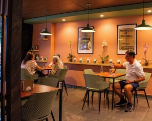 Ein Restaurantinneres mit Tischen, Stühlen, hängenden Lampen und einer Wand mit einem Schild.