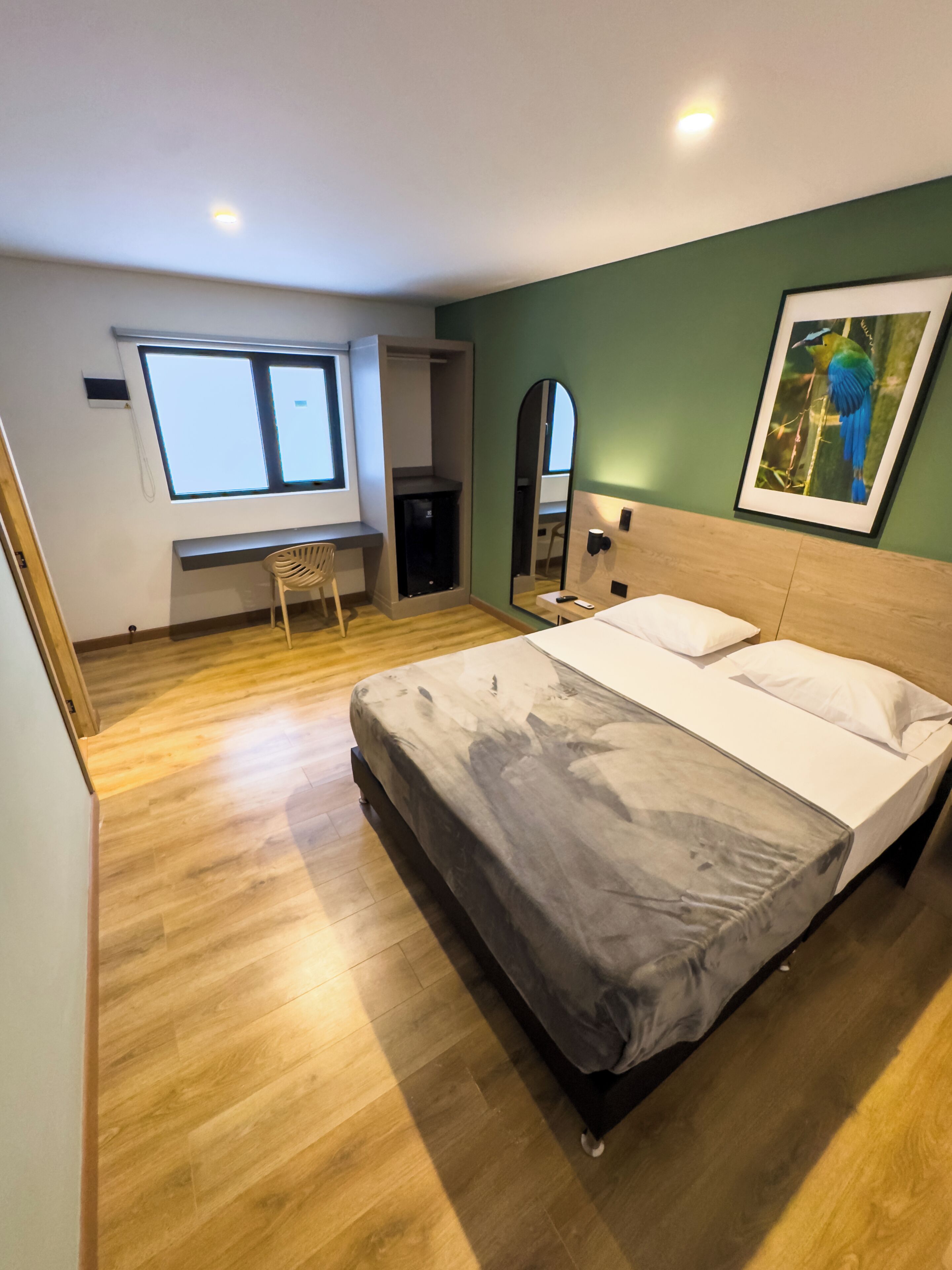 Un dormitorio con cama, escritorio, silla, armario, espejo y ventana.
