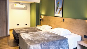 Ein Hotelzimmer mit zwei Betten, einem Holz-Kopfteil, einem gerahmten Bild, einer Klimaanlage und einem Holzboden.