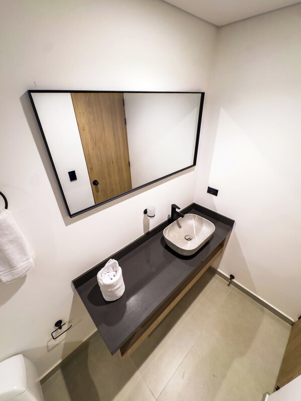 A modern bathroom with a large mirror, a sink, and a towel rack. - Habitat Ochentayuno (Medellín)