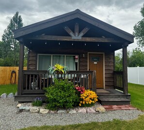 A wooden cabin with a porch, a door, and a window. - The Roost Cabins LLC #1 Near Glacier National Park (Columbia Falls)