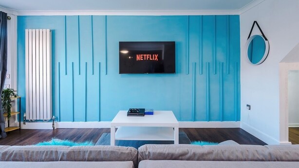 A living room with a TV mounted on a blue wall, a white coffee table, and a sofa. - Spacious 2 Bedroom House | Sleeps 8 | Driveway Parking | Pool Table & Games (Greater Manchester)