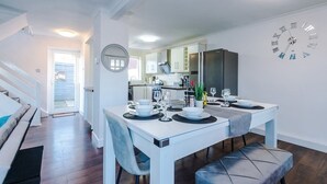 A modern kitchen with a built-in refrigerator, a dining table set for four, and a wall clock. - Spacious 2 Bedroom House | Sleeps 8 | Driveway Parking | Pool Table & Games (Greater Manchester)