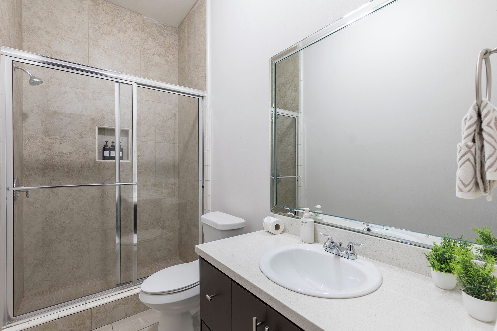 A bathroom with a shower, toilet, sink, and a large mirror.