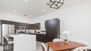 A modern kitchen with dark cabinets, a stainless steel refrigerator, a microwave, and a dining area with a wooden table and white chairs. - Relax in Style – Gated 3BR/2BATH Close to Mall & Restaurants - Centrally Located (McAllen)