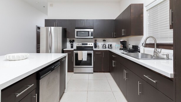 A modern kitchen with stainless steel appliances, dark cabinetry, and a white countertop. - Relax in Style – Gated 3BR/2BATH Close to Mall & Restaurants - Centrally Located (McAllen)