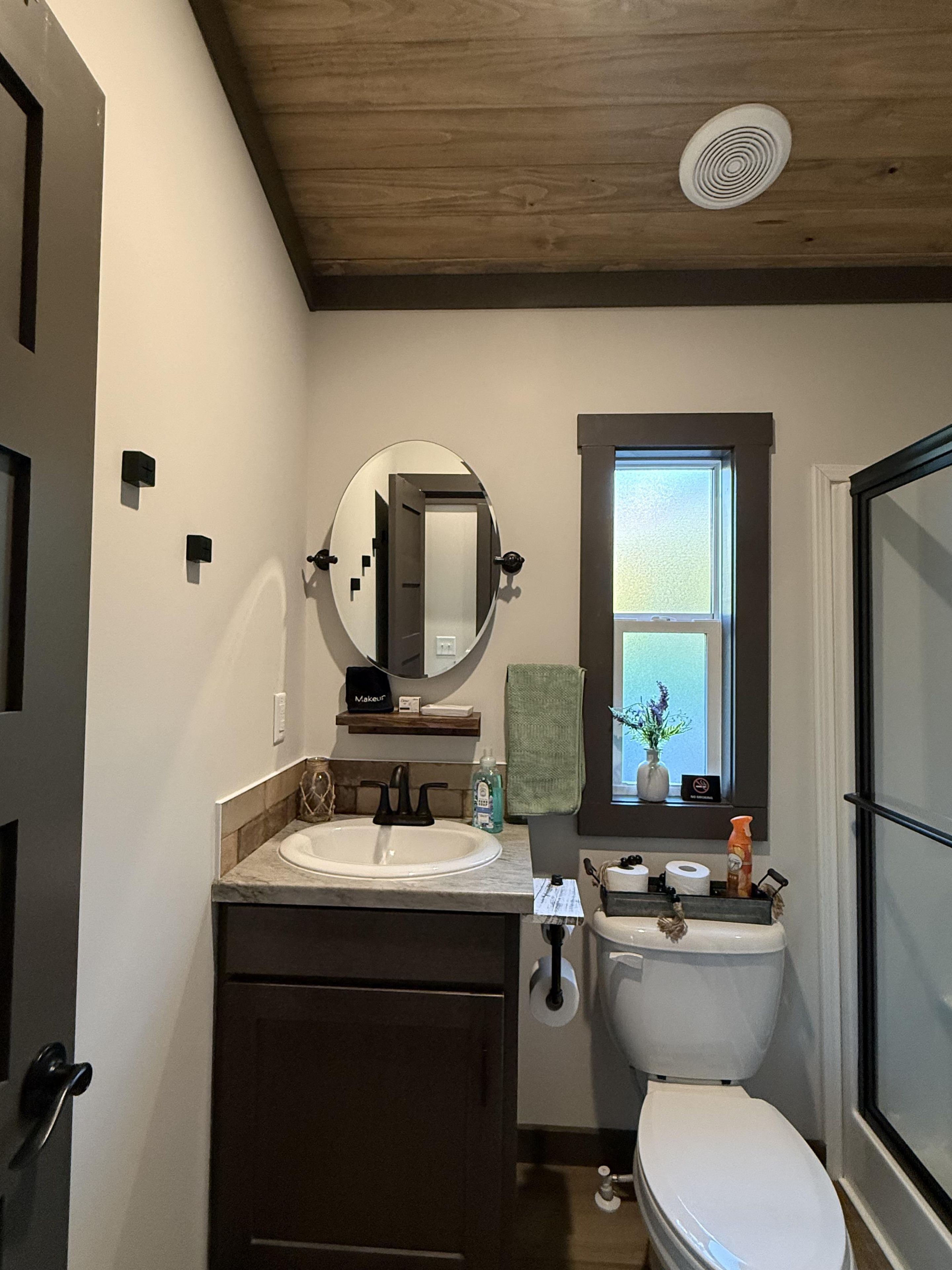 A bathroom with a double sink, a toilet, a mirror, a window, and a shower area.