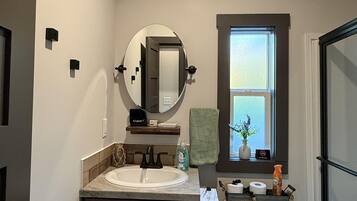 A bathroom with a double sink, a toilet, a mirror, a window, and a shower area.