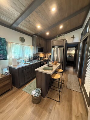 A modern kitchen with a central island, wooden cabinets, a microwave, and a refrigerator. - TJs Lake Getaway - Located 1 Mile from Lake Barkley (Cadiz)