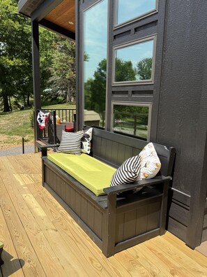 Una terraza de madera con un espacio exterior de estar oscuro, que incluye un banco con cojines y almohadas.