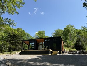 A modern cabin with a covered porch, large windows, and a gravel driveway. - TJs Lake Getaway - Located 1 Mile from Lake Barkley (Cadiz)