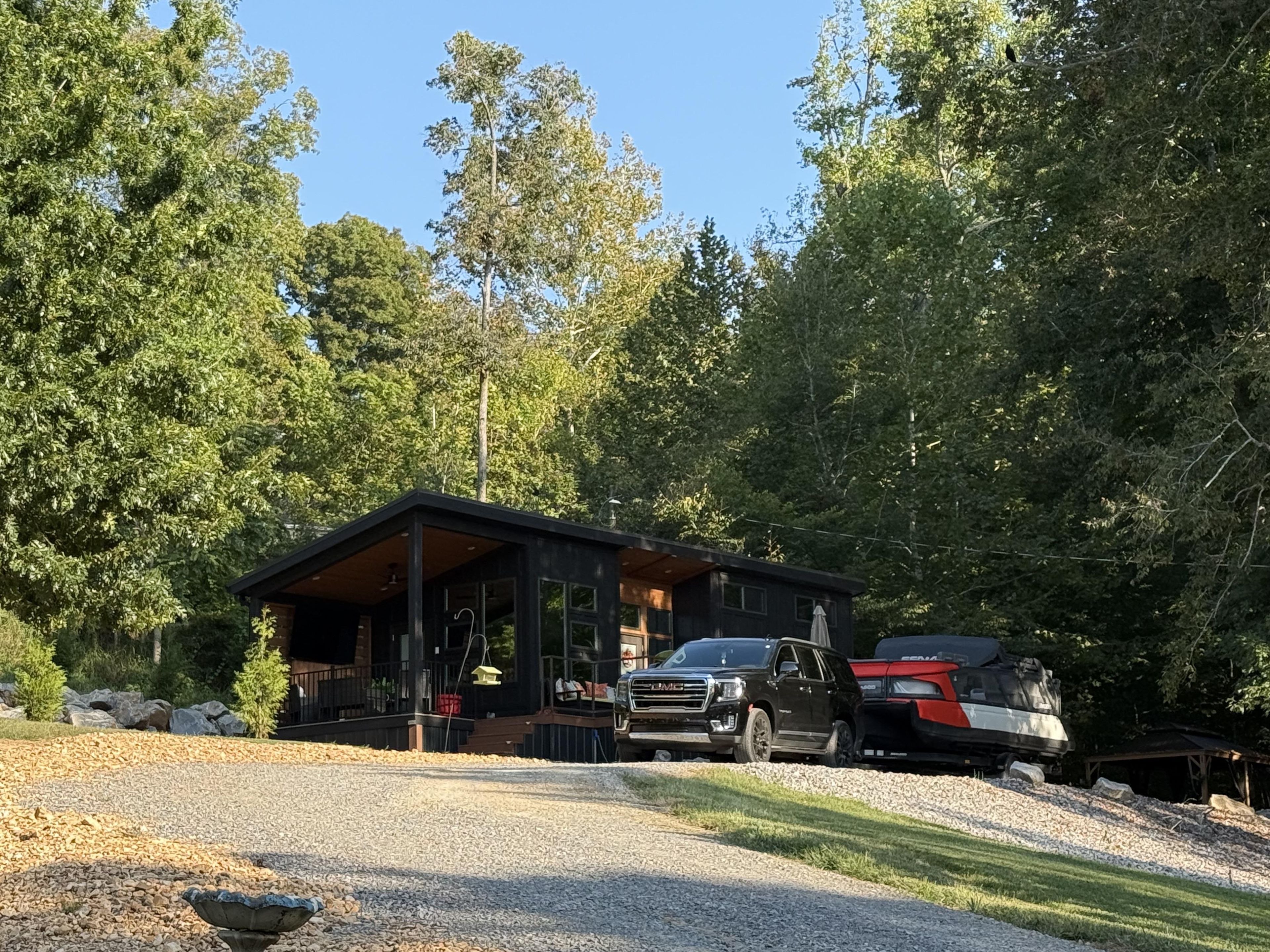 A cabin with a gravel driveway, surrounded by trees.