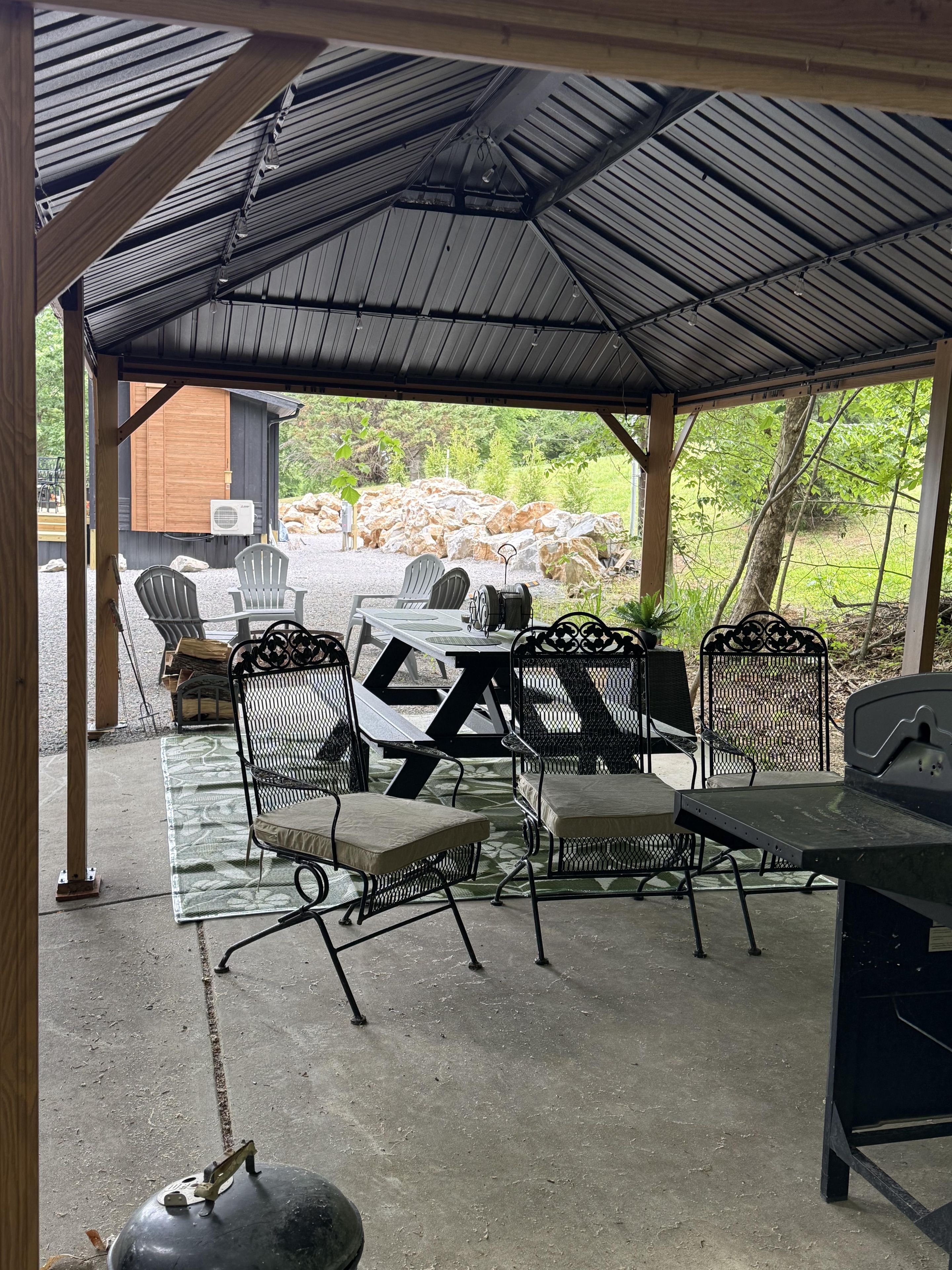 An outdoor patio with a covered seating area, a grill, and a view of the surrounding landscape.