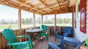 Eine Holzterrasse mit Tisch und Stühlen, großen Fenstern und Blick auf eine grüne Landschaft.