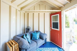 A room with a grey sofa, blue cushions, a red door, a fan, and a blue carpet.