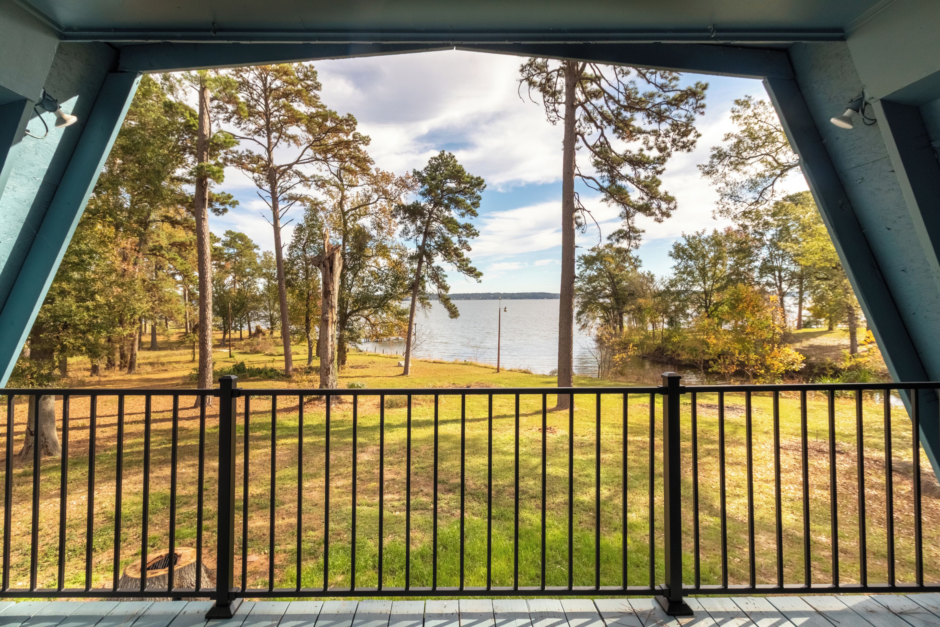 A view from a covered deck with a railing, overlooking a grassy area with trees and a body of water.