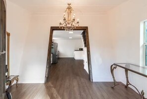 A hallway with a chandelier, wooden flooring, and a view into a kitchen area. - Leave it all behind and relax at Little Ladies Lake House. (Chandler)