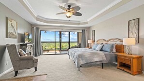 A bedroom with a bed, a chair, a nightstand, a ceiling fan, and a large window with a view. - Sunset Ridge  Private Patio, Cliffside Lake Views (Lake Ozark)