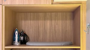 Ein Holzkabinet mit einer Ablagefläche, auf der ein Bügeleisen, eine Mehrfachsteckdose und eine gefaltete Decke liegen.