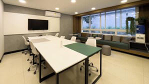 Ein Konferenzraum mit einem langen Tisch, weißen Stühlen, einem Fernseher und einem Fenster mit Pflanzen.