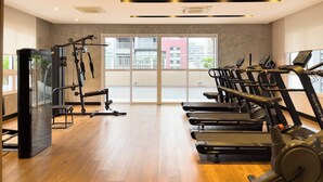 Une salle de sport équipée de matériel d’exercice, dotée d’un plancher en bois et de grandes fenêtres offrant une vue sur les bâtiments.
