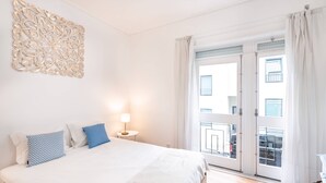 Une chambre d’hôtel avec un lit, un élément décoratif mural, une table de chevet avec une lampe et une vue sur l’extérieur par une porte vitrée.