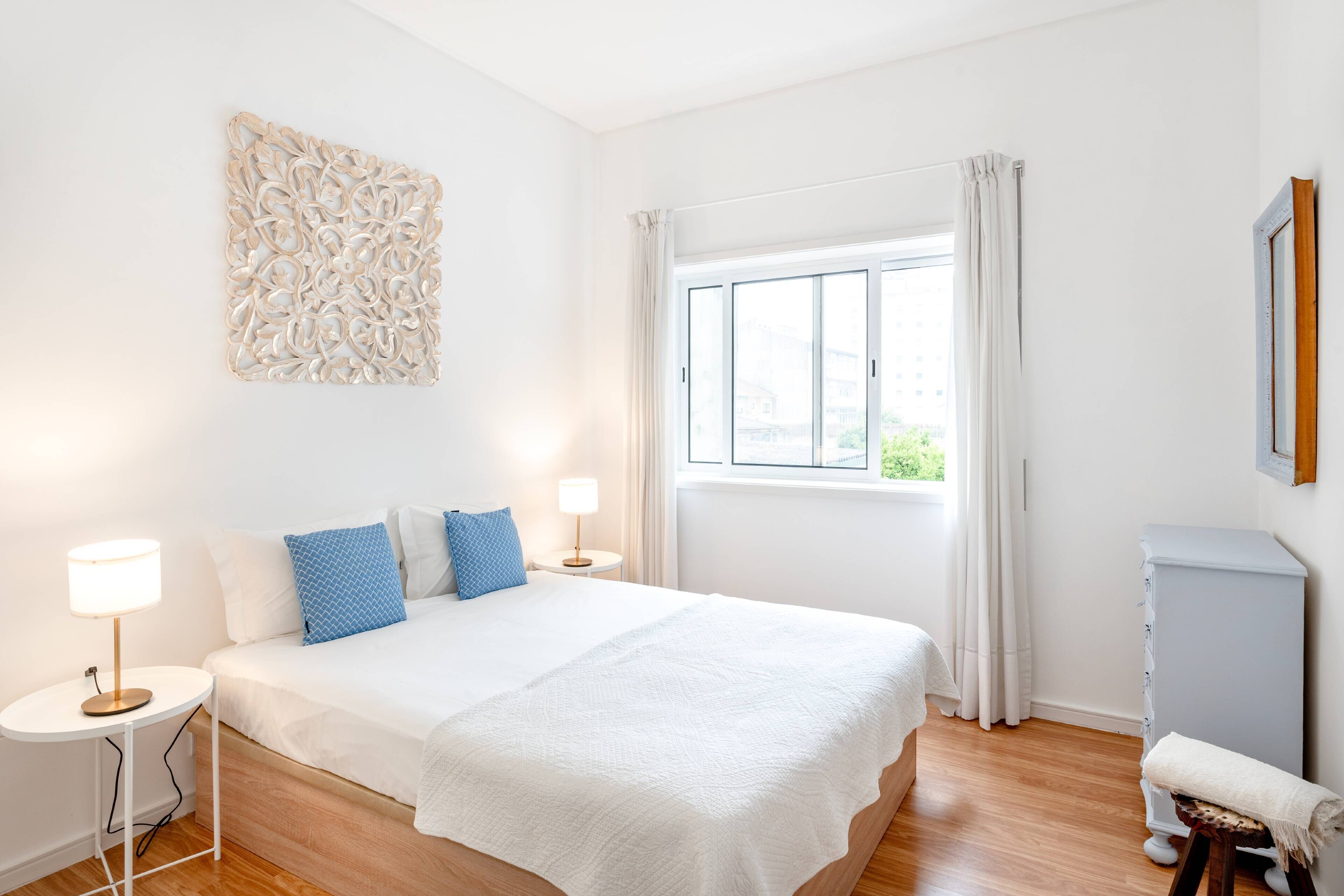 Ein Schlafzimmer mit Bett, Nachttischen, einem Fenster und einer Kommode.
