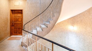 Un escalier en colimaçon, avec une porte en bois en bas, une rampe en métal et un mur à la texture particulière.