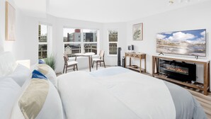Una habitación de hotel moderna con una cama grande, televisión, chimenea y vistas a la ciudad a través de amplias ventanas.
