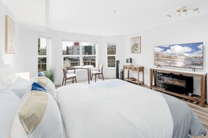 Ein modernes Hotelzimmer mit einem großen Bett, einem Fernseher, einem Kamin und Blick auf die Stadt durch große Fenster.