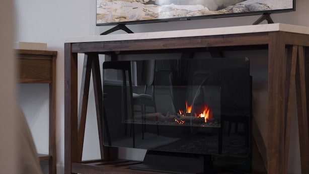 Una chimenea moderna con frente de vidrio, estructura de madera y un televisor de pantalla plana montado encima.