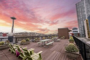 Eine Dachterrasse mit Holzboden, grünen Stühlen, Picknicktischen, Pflanzkübeln mit Grünpflanzen und Blick auf die Space Needle und die Skyline.