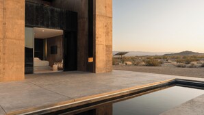 A modern building with a pool, large windows, and a desert landscape view. - Folly Mojave Off-Grid Wilderness Retreat (Twentynine Palms)