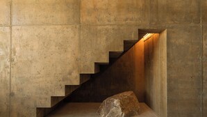 A concrete staircase with a rock at the bottom, leading to a lit area. - Folly Mojave Off-Grid Wilderness Retreat (Twentynine Palms)