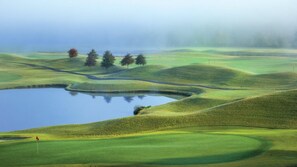 Ein Golfplatz mit sanften grünen Hügeln, einem Teich und vereinzelten Bäumen.