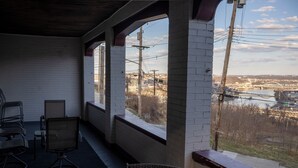 Uma área de estar coberta ao ar livre, com paredes de tijolo, vista para um rio e uma ponte ao longe.