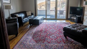 Sala de estar com sofá, banquinho, televisão e tapete estampado.