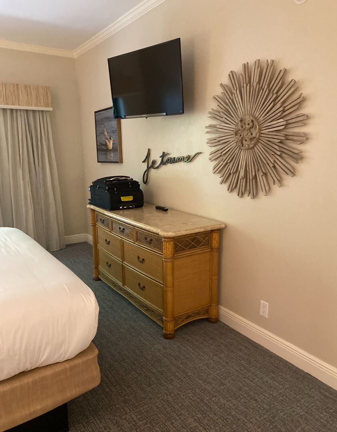 A hotel room with a bed, a dresser, a flat-screen TV, a wall decoration, and a framed picture.