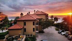 Lomakeskus, jossa on useita rakennuksia, asfaltoitu ajotie ja upea merinäköala auringonlaskun aikaan.