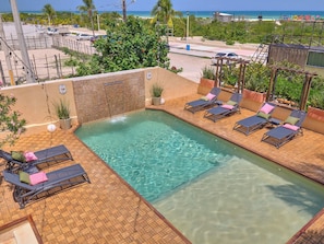 Una piscina en la azotea con sillas de descanso y un muro de piedra.
