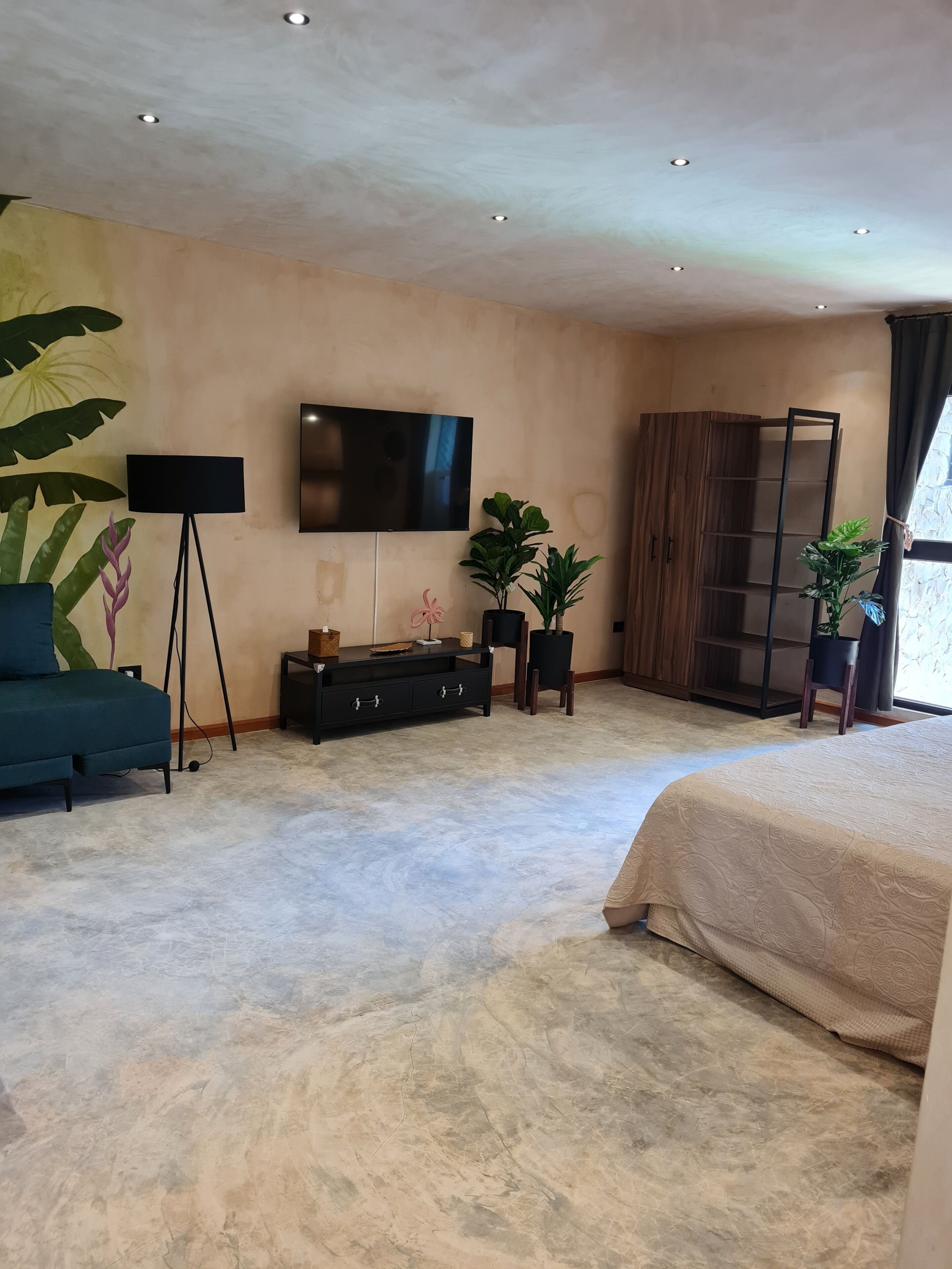 A modern bedroom with a large bed, a TV mounted on the wall, a sofa, and a cabinet.