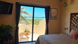 Un dormitorio con cama, televisión, vista al océano y balcón con plantas.