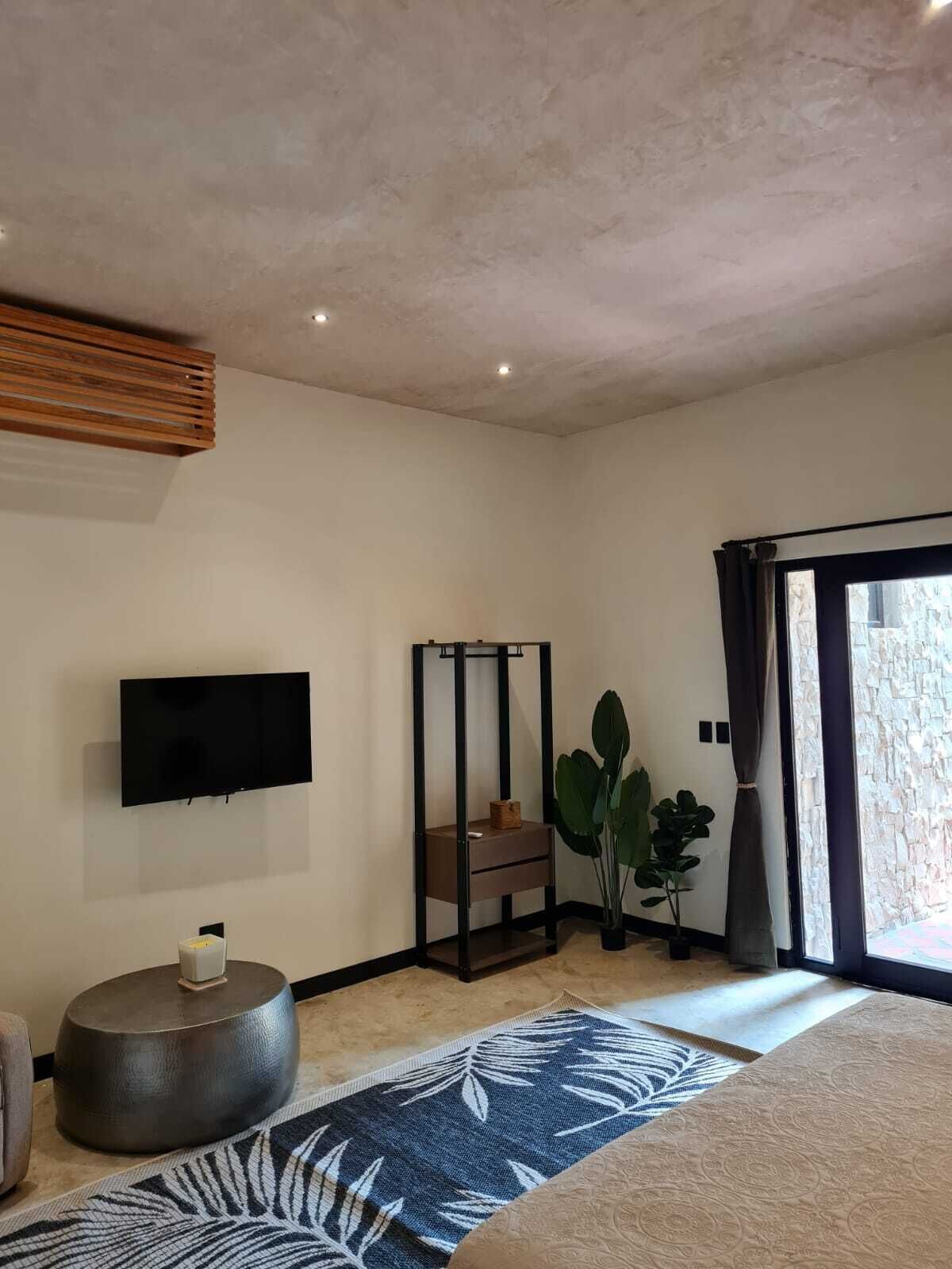Un dormitorio moderno con televisor de pantalla plana, cama plegable, una planta grande en maceta y vistas a través de una puerta de cristal.