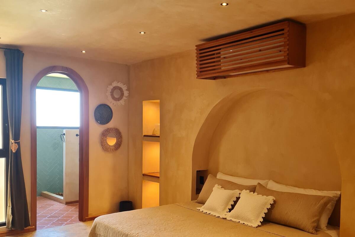 A bedroom with a large bed, an arched ceiling, and a door leading to a balcony.