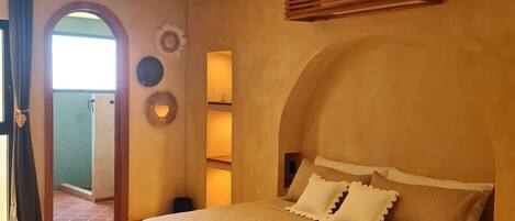 Ein Schlafzimmer mit einem großen Bett, einer gewölbten Decke und einer Tür, die auf einen Balkon führt.